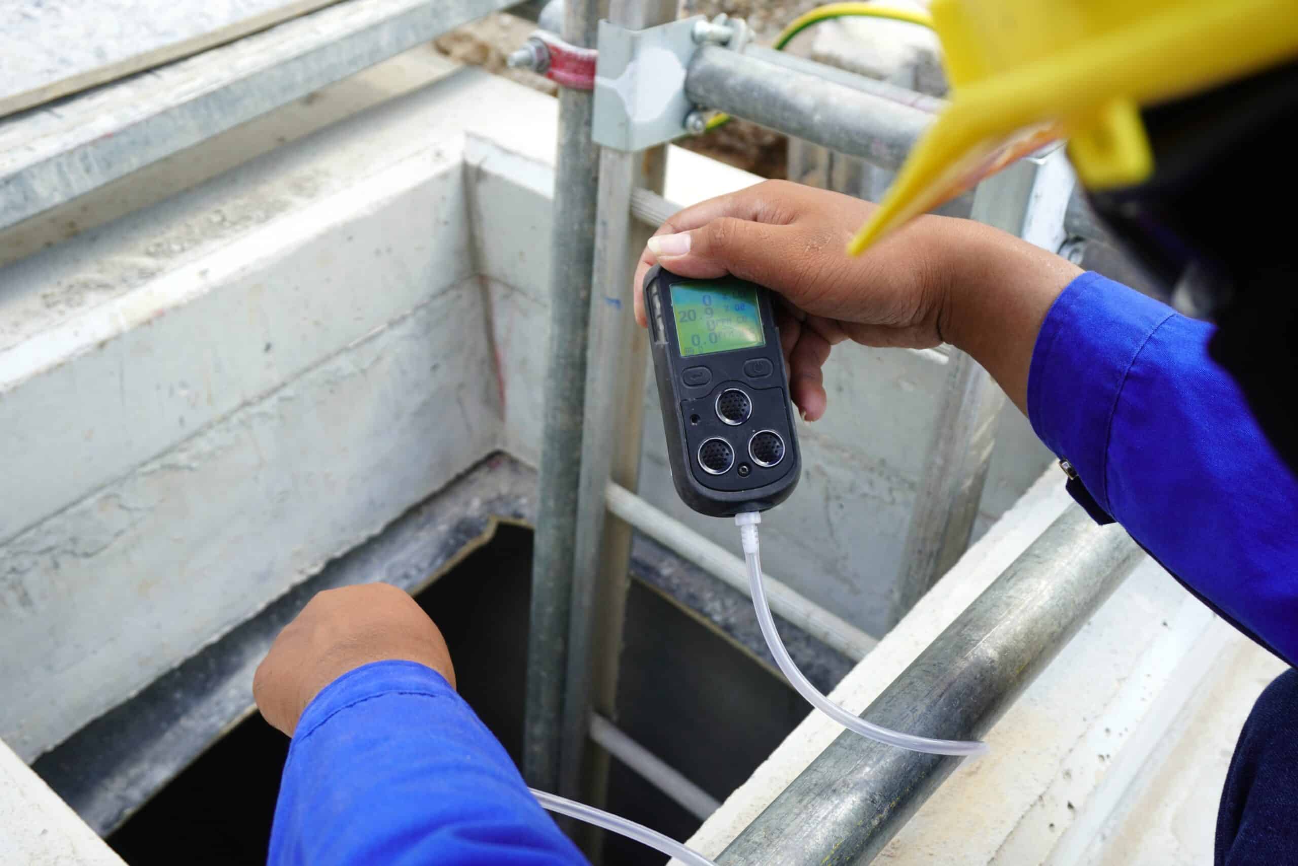 Construction supervisor hand holding gas detector device while commencing safety gas testing atmosphere at manhole to work construction site